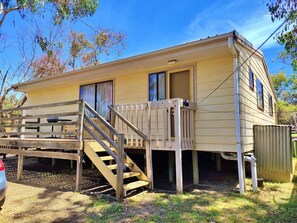 A single-story mobile home with a wooden deck and a staircase leading to the entrance.