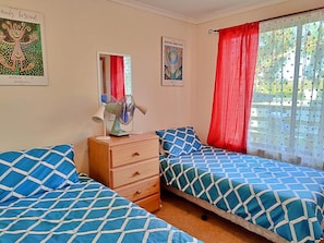 A bedroom with two beds, a wooden dresser, a mirror, and artwork on the walls.