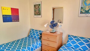 A bedroom with two beds, a wooden dresser, a mirror, and wall art.