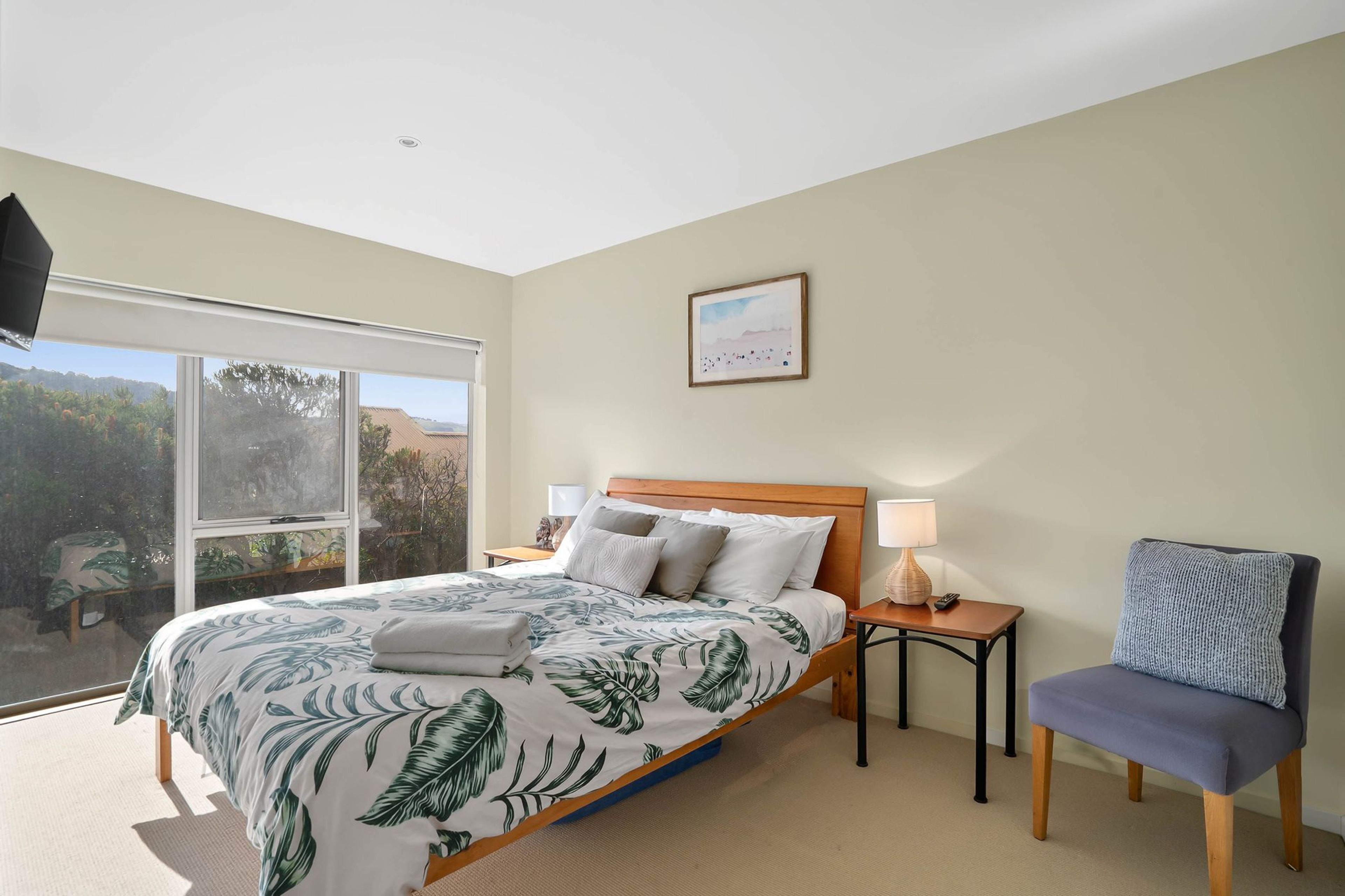 Une chambre d’hôtel avec un lit, une chaise, une table de chevet, une lampe et un tableau au mur.