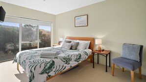 Una habitación de hotel con cama, una silla, una mesita de noche, una lámpara y un cuadro en la pared.