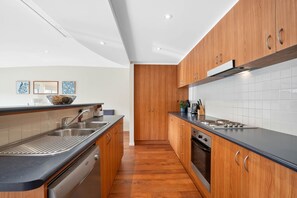 A modern kitchen with wooden cabinets, a black countertop, stainless steel appliances, and a tiled backsplash. - Butter Factory 9 (Apollo Bay)