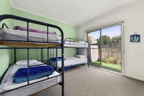 Ein Schlafsaalzimmer mit Etagenbetten, einer großen Schiebeglas-Tür zum Balkon und Blick ins Freie.