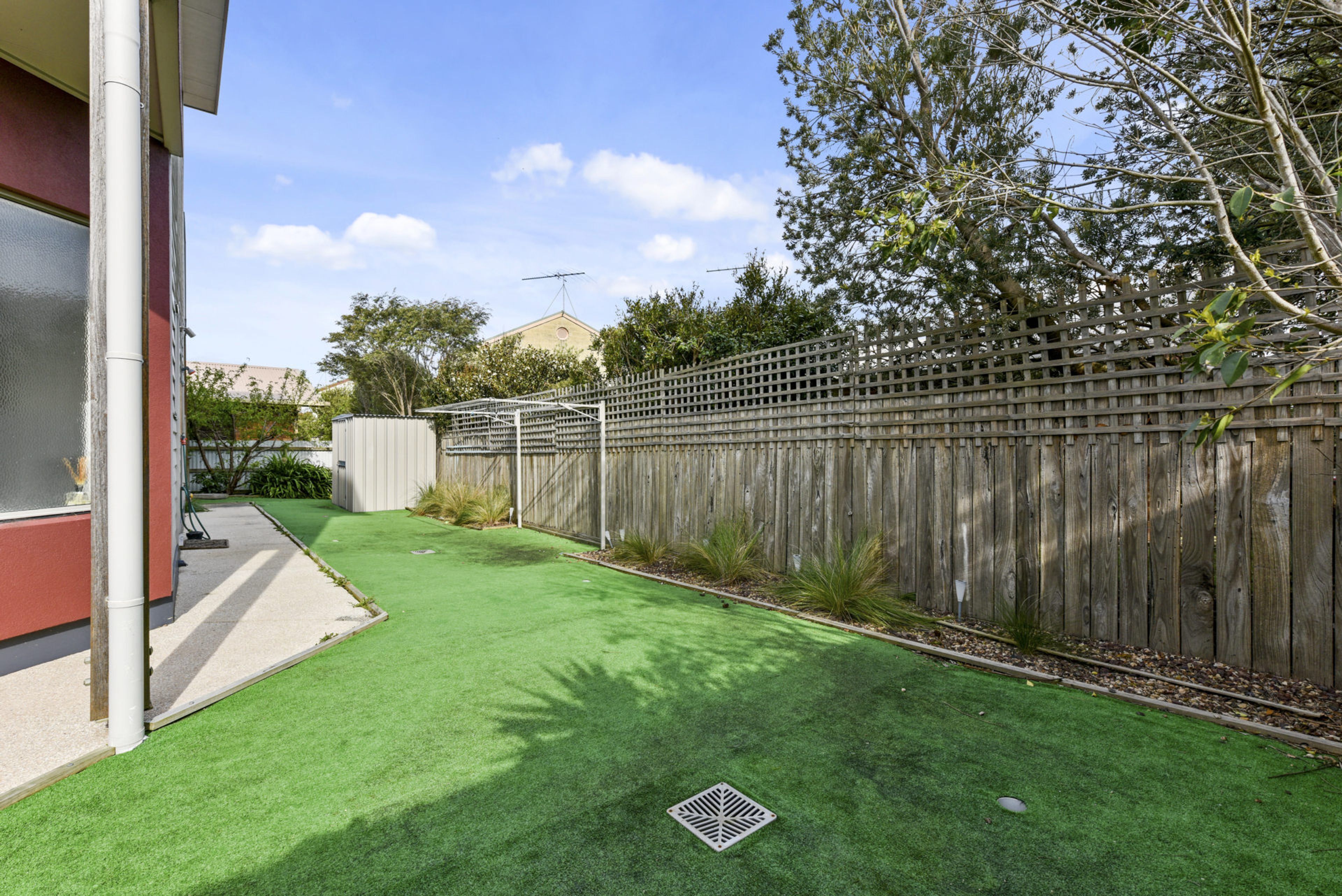 A backyard with artificial grass, a wooden fence, and a utility box.