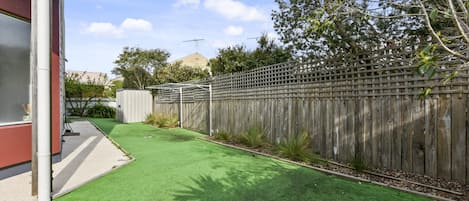 A backyard with artificial grass, a wooden fence, and a utility box.