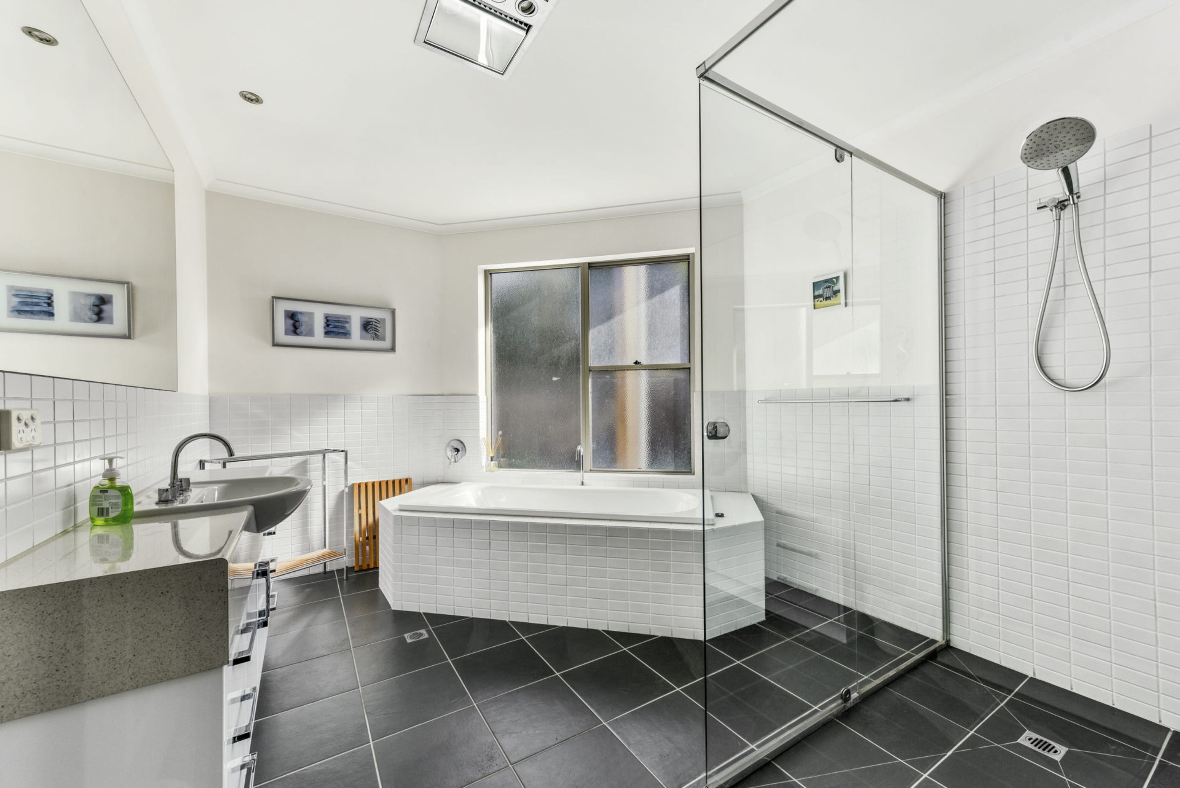 Une salle de bain moderne avec une douche à l’italienne, une baignoire sur pieds et une grande fenêtre.