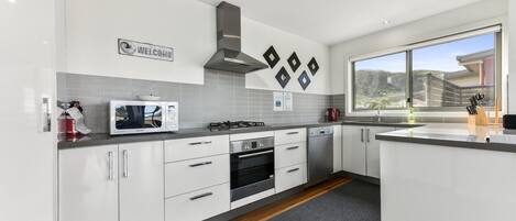 A modern kitchen with white cabinets, a built-in microwave, a gas stove, and a stainless steel range hood.