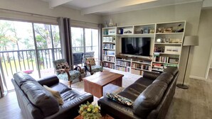 Un salon doté d’une grande télévision, de bibliothèques et d’un balcon aménagé avec du mobilier d’extérieur.