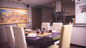 Un comedor con una mesa de madera oscura, sillas blancas acolchadas y un mantel individual colorido. Hay copas de vino y platos sobre la mesa.