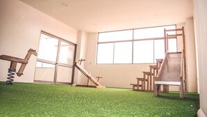 Una habitación con césped artificial, una escalera de madera, un columpio de madera y un tobogán de madera.