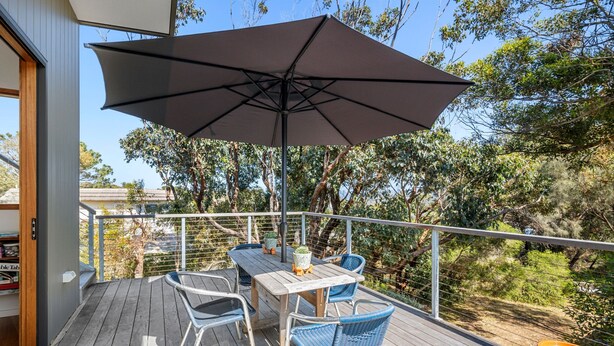 Une terrasse en bois avec une table et des chaises, un parasol et une plante en pot.