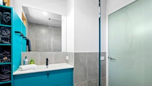 Une salle de bain avec un meuble-lavabo bleu, un miroir, un évier et une porte de douche en verre.