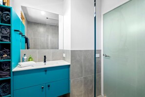 Une salle de bain avec un meuble-lavabo bleu, un miroir, un évier et une porte de douche en verre.