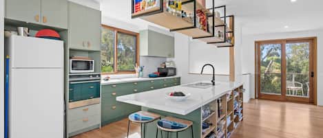 A modern kitchen with a central island, bar stools, and a built-in bookshelf.