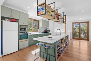 A modern kitchen with a central island, bar stools, and a built-in bookshelf. - Steppy Beach Retro (Aireys Inlet)