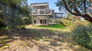 Une maison à deux étages avec un balcon, entourée d’arbres et bordée d’une pelouse.