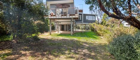 A two-story house with a balcony, surrounded by trees and a grassy yard.