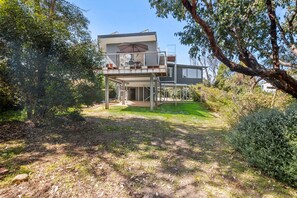 Une maison à deux étages avec un balcon, entourée d’arbres et bordée d’une pelouse.