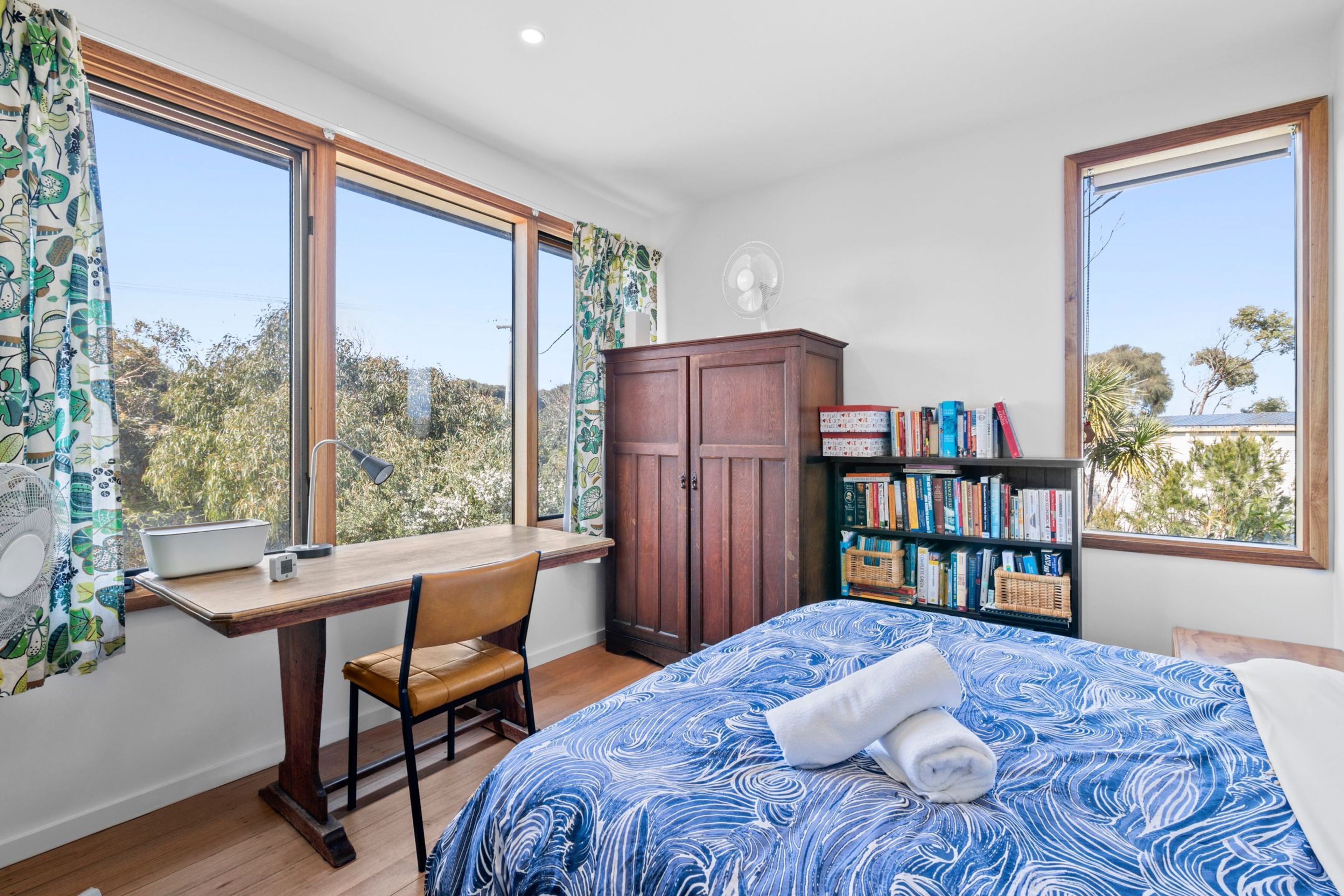 A bedroom with a bed, a desk, a chair, a wardrobe, and a bookshelf.