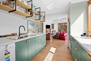 A modern kitchen with a central island, built-in shelves, and a dining area with a sofa and table. - Steppy Beach Retro (Aireys Inlet)