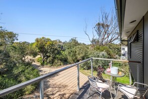 A balcony with a table and chairs, overlooking a garden and trees. - Steppy Beach Retro (Aireys Inlet)