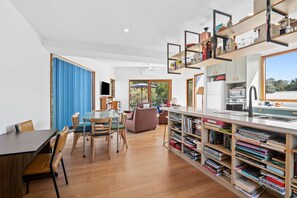 Une cuisine moderne dotée d’appareils électroménagers intégrés, un coin repas avec une table et des chaises en bois, et une bibliothèque remplie de livres.