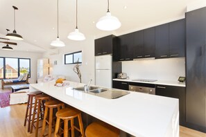 A modern kitchen with a large island, black cabinets, stainless steel appliances, and wooden stools.
