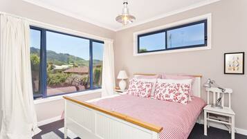 A bedroom with a large window, a bed with floral bedding, a bedside table with a lamp, and a framed picture on the wall.