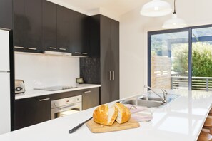 Eine moderne Küche mit dunklen Schränken, einer weißen Arbeitsplatte und einem großen Fenster.