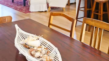 A dining area with a wooden table, chairs, and a woven basket with seashells.