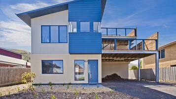 A modern two-story house with a flat roof, large windows, and a covered outdoor area.