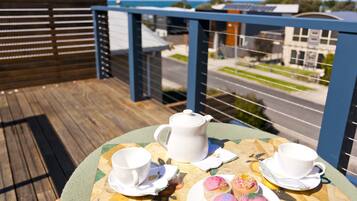 A table with a teapot, cups, saucers, and cupcakes on a deck with a view of a street and buildings.