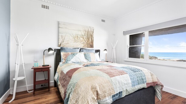 A bedroom with a bed, a nightstand, a lamp, a window with a view of the ocean, and a painting on the wall. - Absolute Beachfront Views Apollo Bay (Apollo Bay)