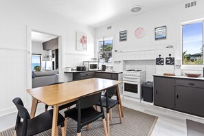 A modern kitchen with a dining area, white cabinetry, and a view of the sea. - Absolute Beachfront Views Apollo Bay (Apollo Bay)