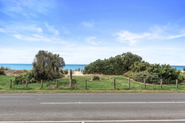 A coastal road with a grassy verge, a wooden fence, and a clear view of the sea.