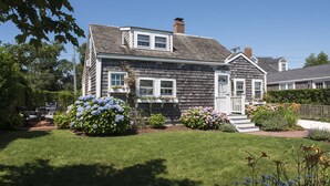 A two-story house with a front porch, a chimney, and a well-maintained garden with hydrangeas and other flowers. - Renovated Cottage off Main Street- Great Location (Nantucket)