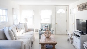 A bright living room with a white sofa, a wooden coffee table, and a television on a white cabinet. - Renovated Cottage off Main Street- Great Location (Nantucket)