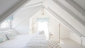 A high-ceilinged, white-themed attic bedroom with a bed, a tufted ottoman, and a hanging light fixture. - Renovated Cottage off Main Street- Great Location (Nantucket)