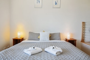 A neatly made bed with a patterned bedspread, two pillows, two bedside lamps, and two folded towels on the bed.