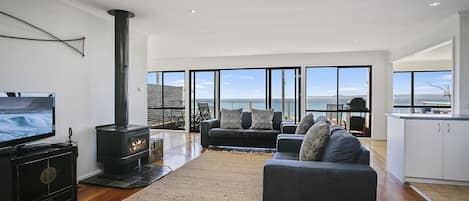Una sala moderna con una televisión grande, chimenea, sofá y vista al mar.