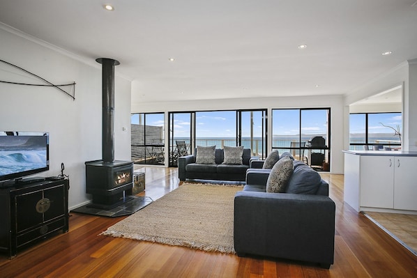 A modern living room with a large TV, a fireplace, a sofa, and a view of the sea.
