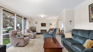 A spacious living room with a large window, a dark-colored sofa, a wooden coffee table, and a television.