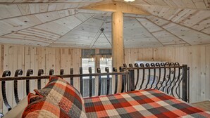 Une chambre rustique aux murs et au plafond en bois, avec un cadre de lit en métal et une couvre-lit à carreaux.