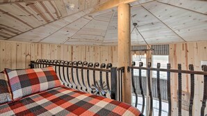 Une pièce avec un plafond en bois, un lit recouvert d’une couverture à carreaux et une vue sur l’extérieur par une fenêtre.