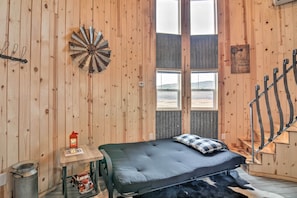 Una stanza in legno con un letto, un tavolino con una lanterna, un bersaglio da freccette e una finestra vista.