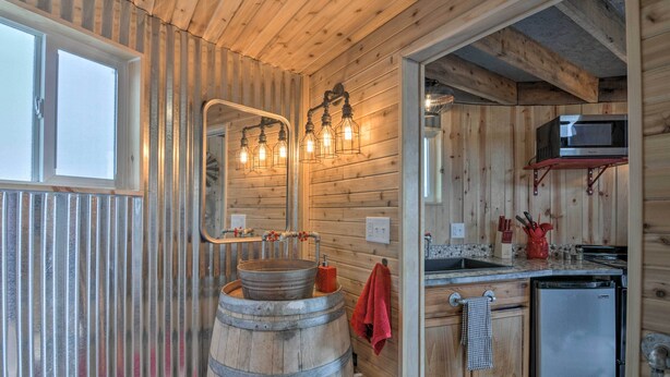 Une cuisine rustique avec des murs en bois, un évier en forme de tonneau en bois, un réfrigérateur en acier inoxydable et un four à micro-ondes posé sur une étagère.