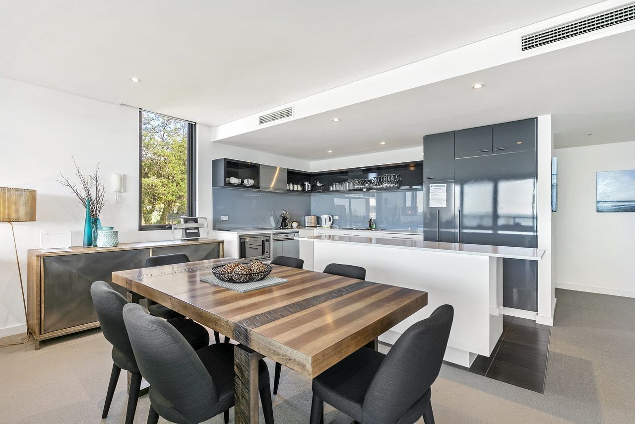 A modern kitchen with integrated appliances, a dining area with a wooden table and chairs, and a large window providing natural light.