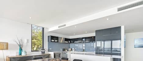 A modern kitchen with integrated appliances, a dining area with a wooden table and chairs, and a large window providing natural light.