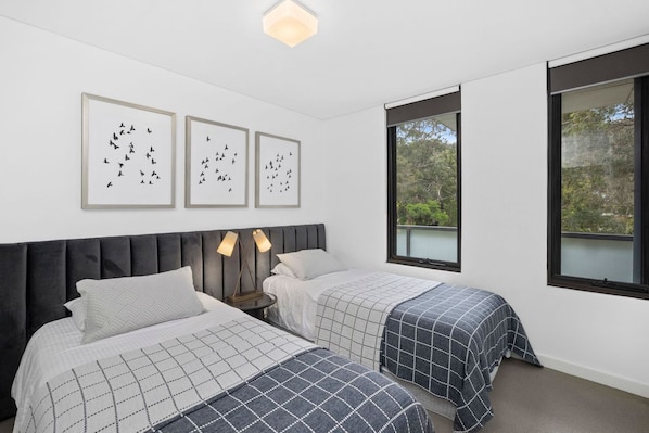 A bedroom with two beds, a large window, and three framed pictures on the wall.
