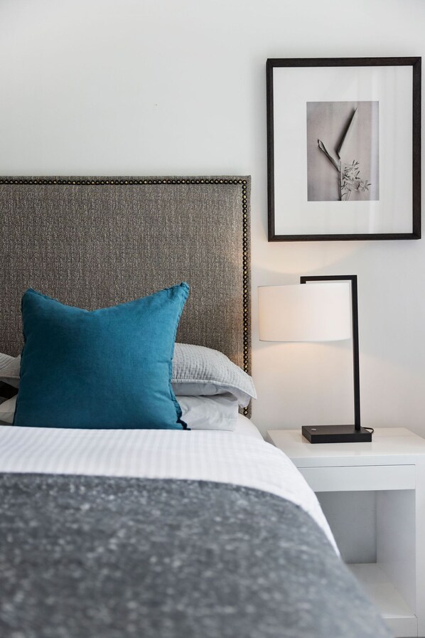 A neatly made bed with a grey and white duvet, a teal pillow, and a textured grey headboard.